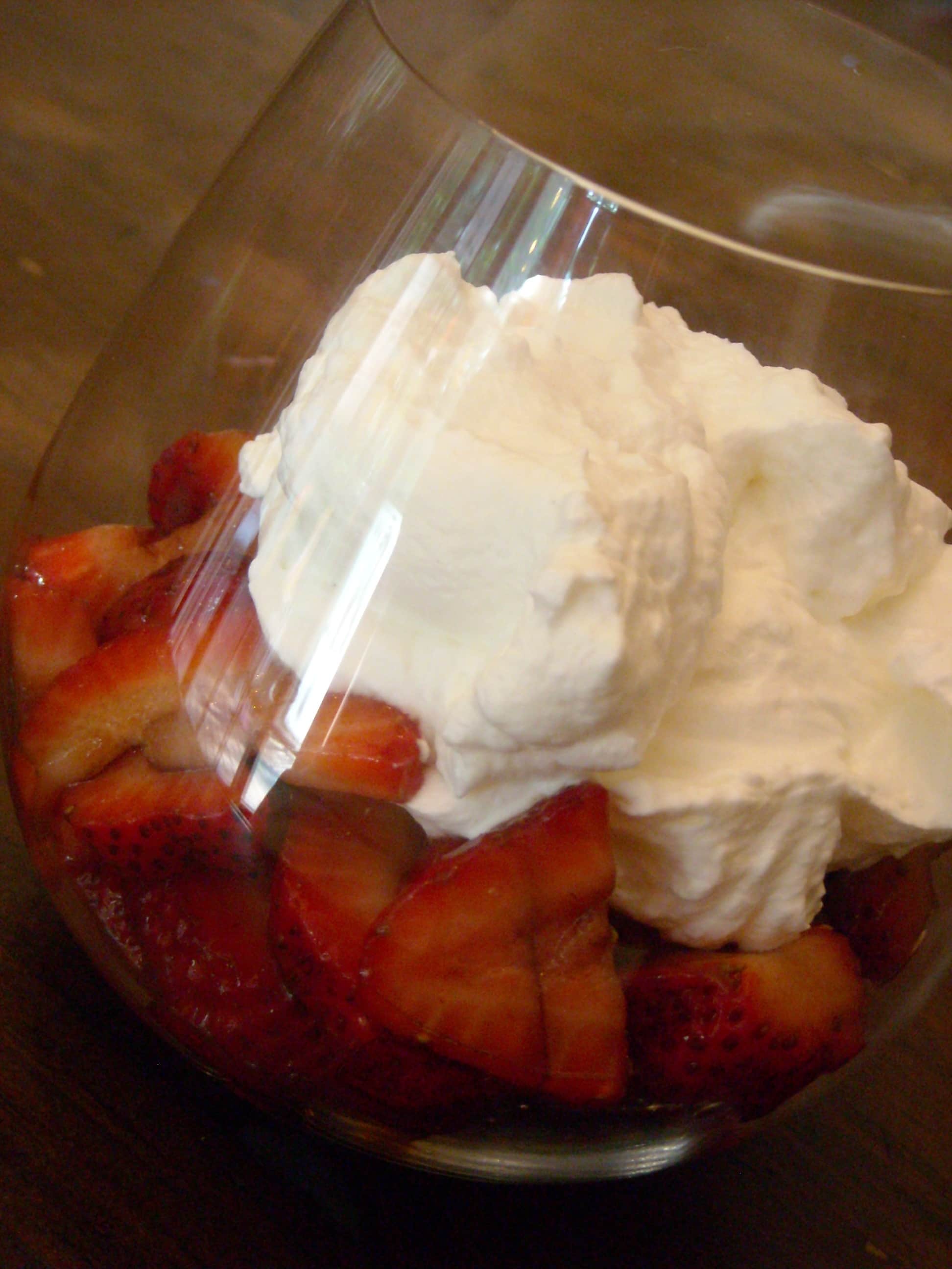 Balsamic Strawberries in a glass topped with fresh whipped cream.
