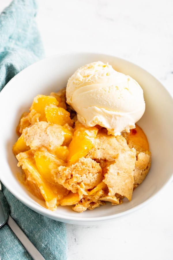 a white bowl filled with frozen peach cobbler and vanilla ice cream