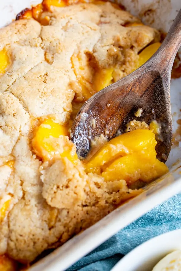 frozen peach cobbler in the baking dish with a wooden spoon