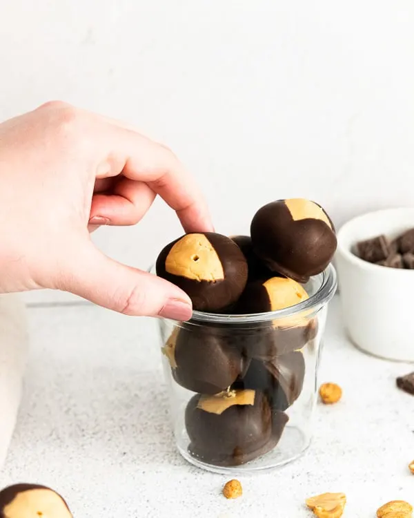 peanut butter buckeyes in a jar with a hand reaching to take one