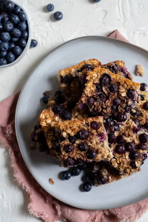 baked blueberry oatmeal cut into squares on a white plate with fresh blueberries