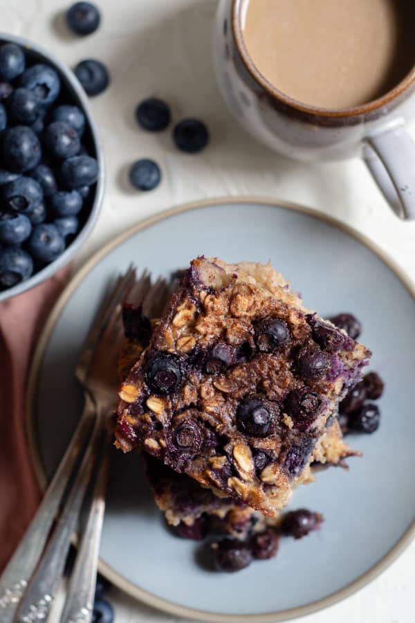 baked blueberry oatmeal sliced on a plate with fresh blueberries and coffee