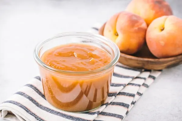 vanilla honey peach butter in a glass jar with peaches in the background