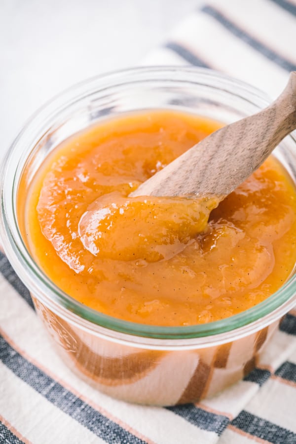 Vanilla honey peach butter in a small glass jar with a small wooden knife.