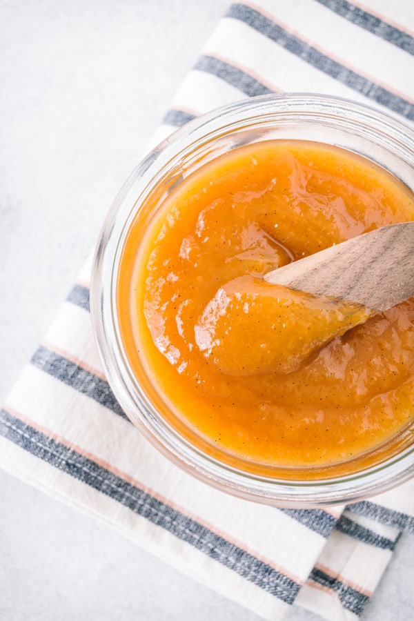Vanilla honey peach butter in a glass jar with a wooden knife.