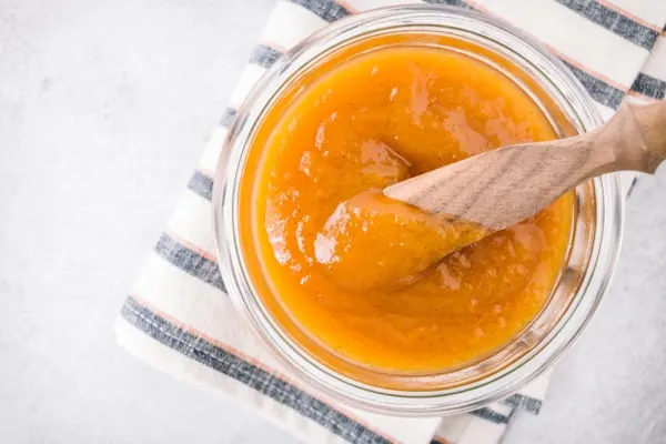 Vanilla honey peach butter in a jar with a wooden knife.