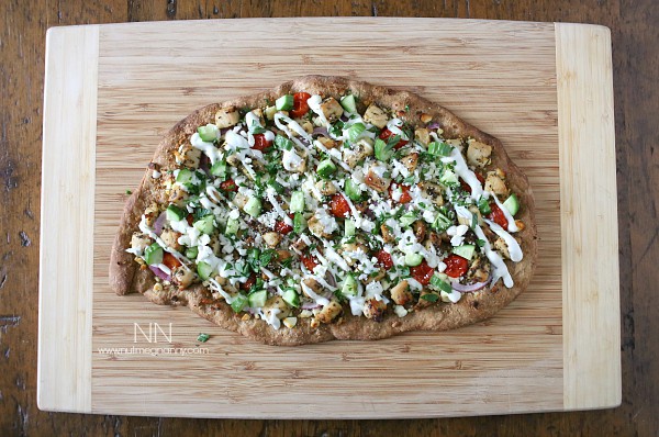 Chicken Souvlaki Pizza on a cutting board drizzled with sauce. 