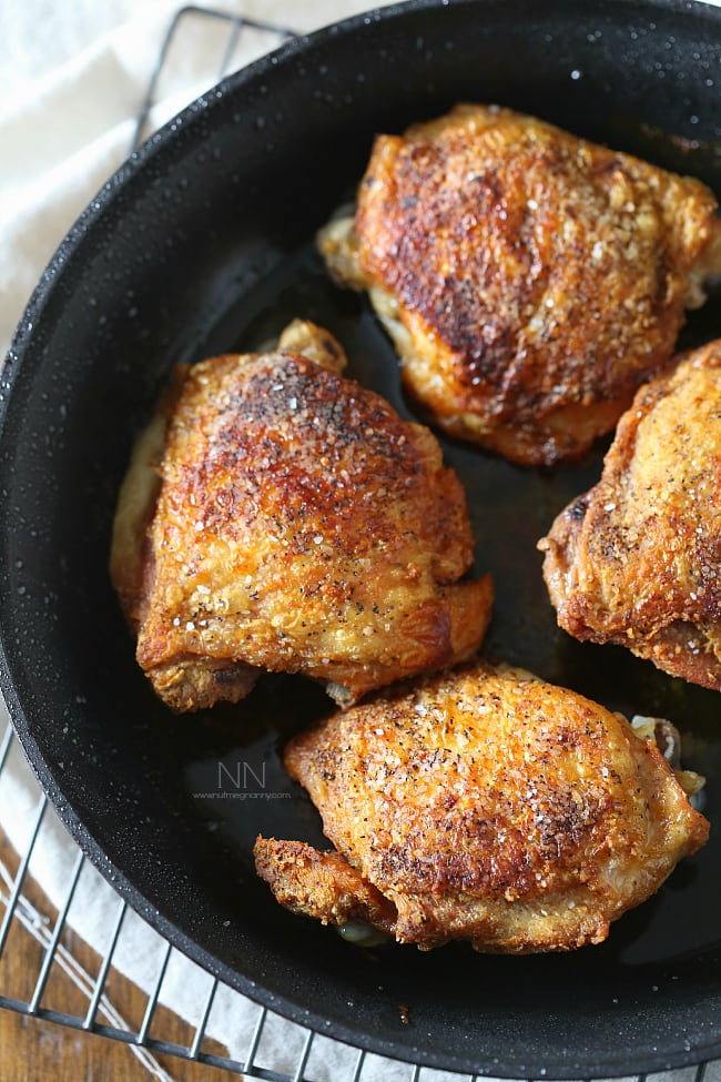 Crispy pan roasted chicken thighs in a skillet sprinkled with kosher salt.