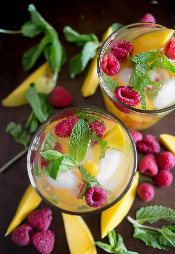 raspberry mango sangria in a glass with fruit around the glasses on a tray