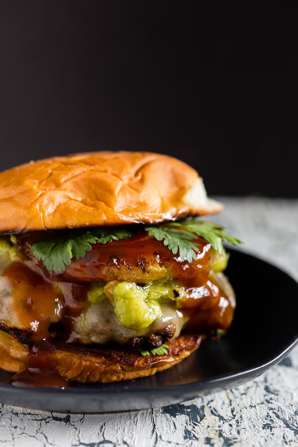 bbq pineapple burger on a plate topped with pineapple, avocado, and bbq sauce.
