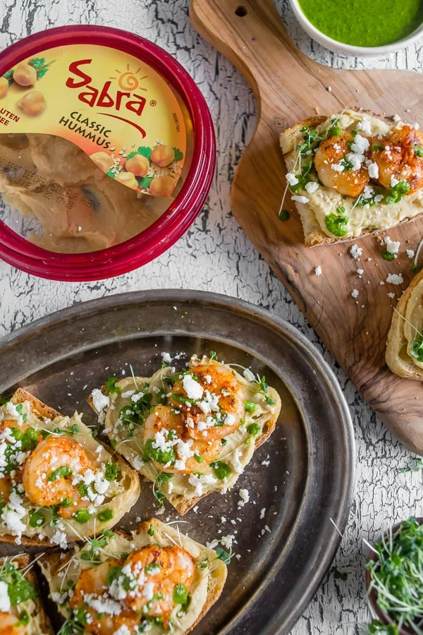 This cajun shrimp hummus crostini is the perfect summer appetizer. Toasted bread topped with hummus, micro greens, spicy cajun shrimp, cilantro pesto and a sprinkling of feta cheese. Hello, summer!
