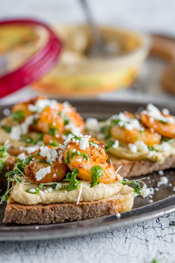 This cajun shrimp hummus crostini is the perfect summer appetizer. Toasted bread topped with hummus, micro greens, spicy cajun shrimp, cilantro pesto and a sprinkling of feta cheese. Hello, summer!