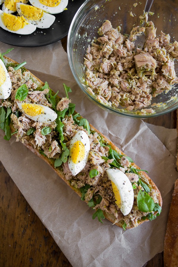 Pesto Tuna Baguette Sandwich sitting on a table topped with hard boiled eggs. 