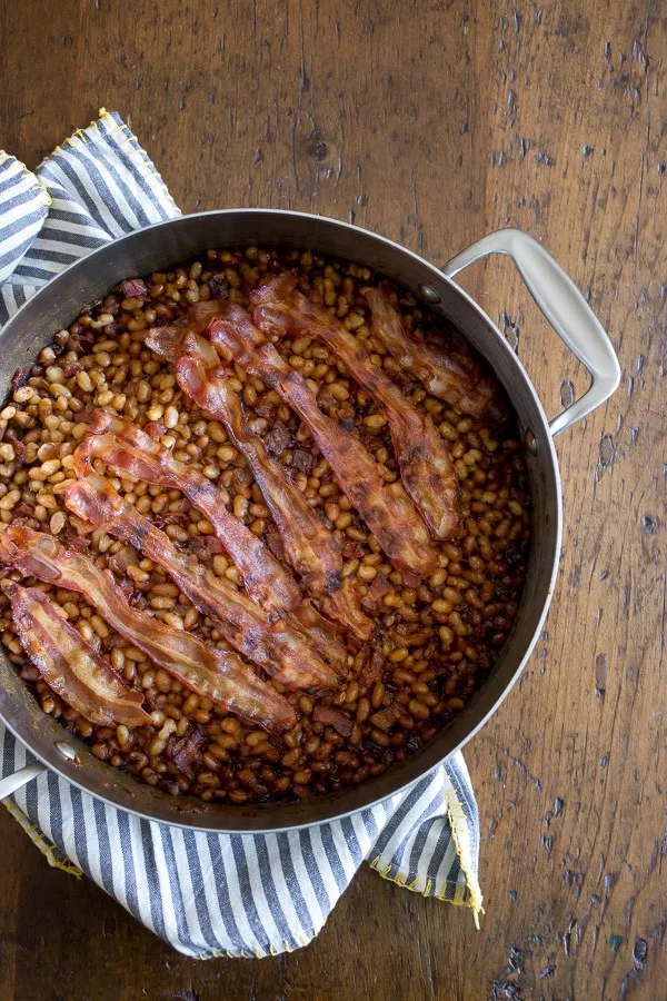 molasses bacon baked beans in a large pan with strips of bacon on top