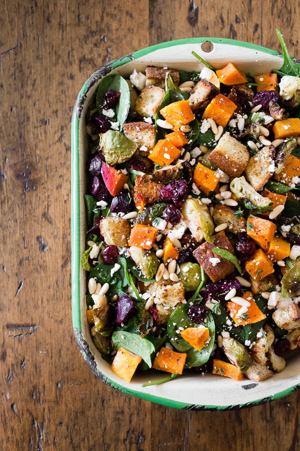 This fall panzanella salad is packed full of fresh roasted vegetables, dried cranberries, pine nuts, feta cheese, buttery toasted gluten free bread and drizzled with a maple syrup herb vinaigrette. This salad is 100% fall and perfect for the holidays! 