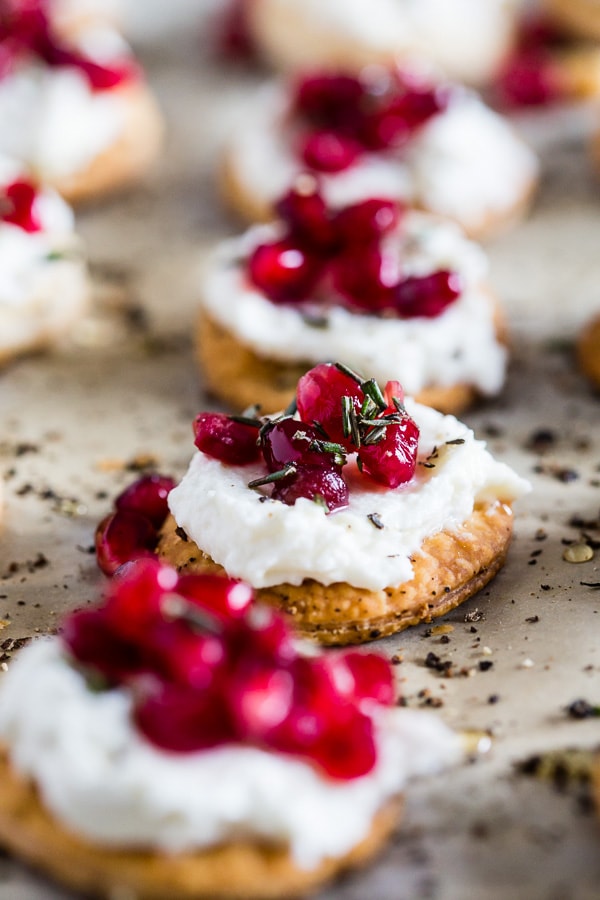 These beautiful whipped goat cheese pomegranate bites are made in less than 30 minutes and are the perfect stunning holiday appetizer. Store bought pie crust is cut out and baked into little flakey cracker rounds and topped with honeyed whipped goat cheese, pomegranate seeds and a sprinkling of honey and rosemary. You will love this new quick and easy holiday appetizer! 