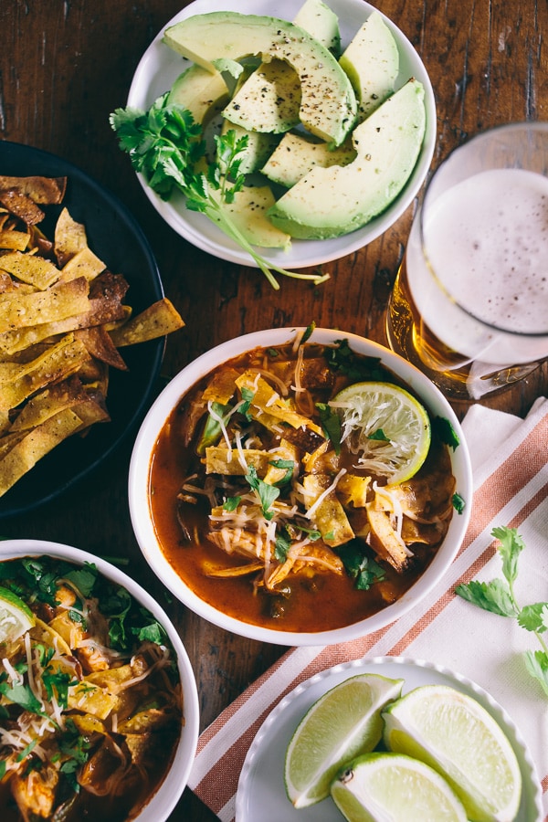 chicken and chard tortilla soup in a bowl surrounded by toppings and a beer