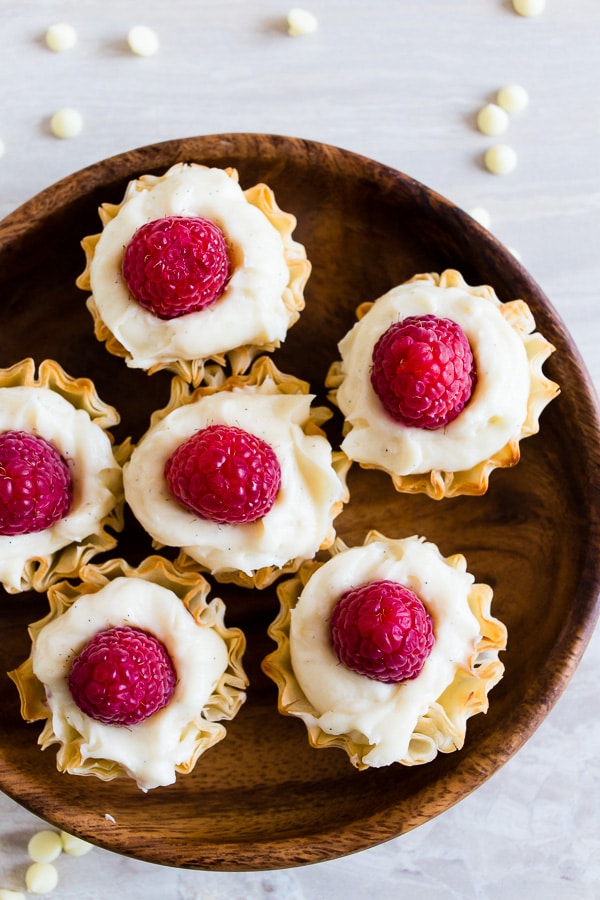 These no bake white chocolate cheesecake phyllo bites are perfectly adorable and topped with fresh raspberries. They are super simple to make and would look perfect on your holiday dessert table.