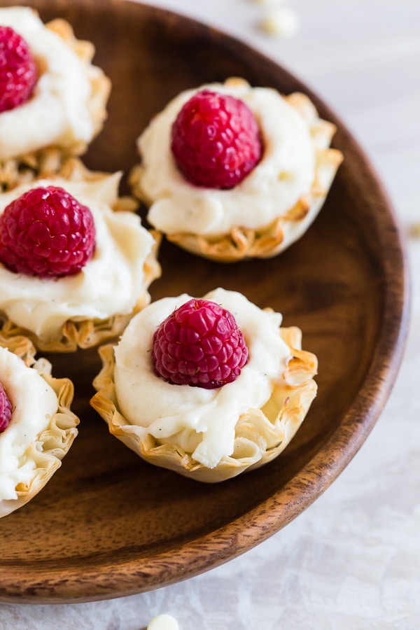 These no bake white chocolate cheesecake phyllo bites are perfectly adorable and topped with fresh raspberries. They are super simple to make and would look perfect on your holiday dessert table.