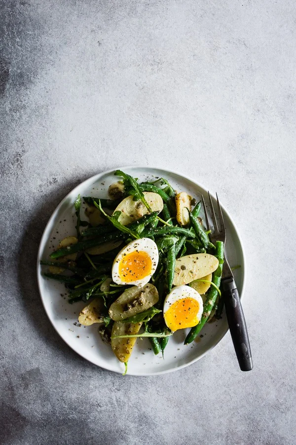This tangy green bean potato salad is the perfect combination of buttery fingerling potatoes, crunchy blanched green beans, peppery arugula and soft boiled eggs all tossed in a creamy Dijon and caper vinaigrette. It's tangy, perfect for hot summer nights and makes an amazingly fast and easy meatless dinner! 