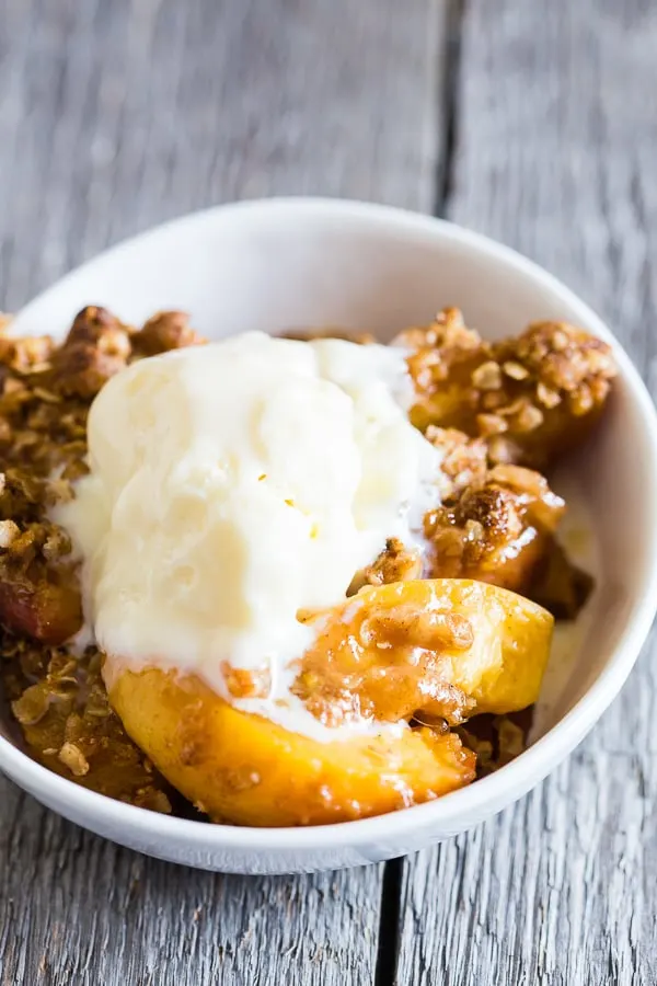 giner peach crisp scooped into a bowl and topped with ice cream