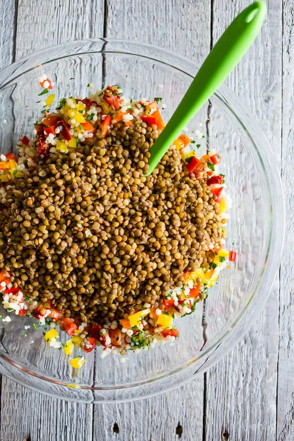 Lentils, couscous and veggies in bowl with a green mixing spoon sticking out.