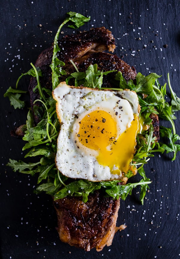 fried egg topped grilled steak with arugula leaves under the egg