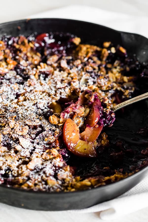 blueberry peach cast iron crisp with a spoon in the cast iron skillet. 