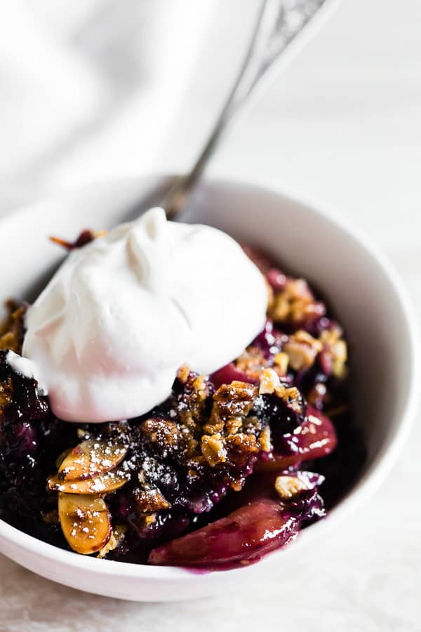 blueberry peach cast iron crisp in a bowl topped with whipped cream. 