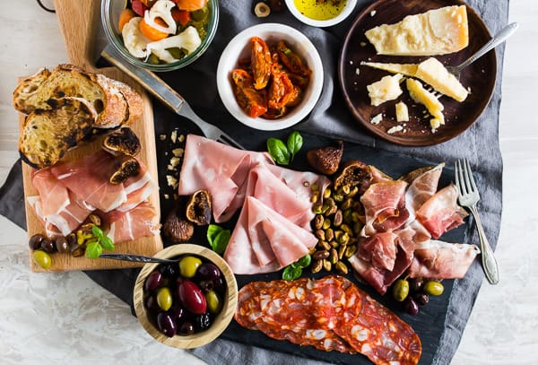 Overhead view of Italian charcuterie board with meats, cheese, olives, nuts, bread and tomatoes.