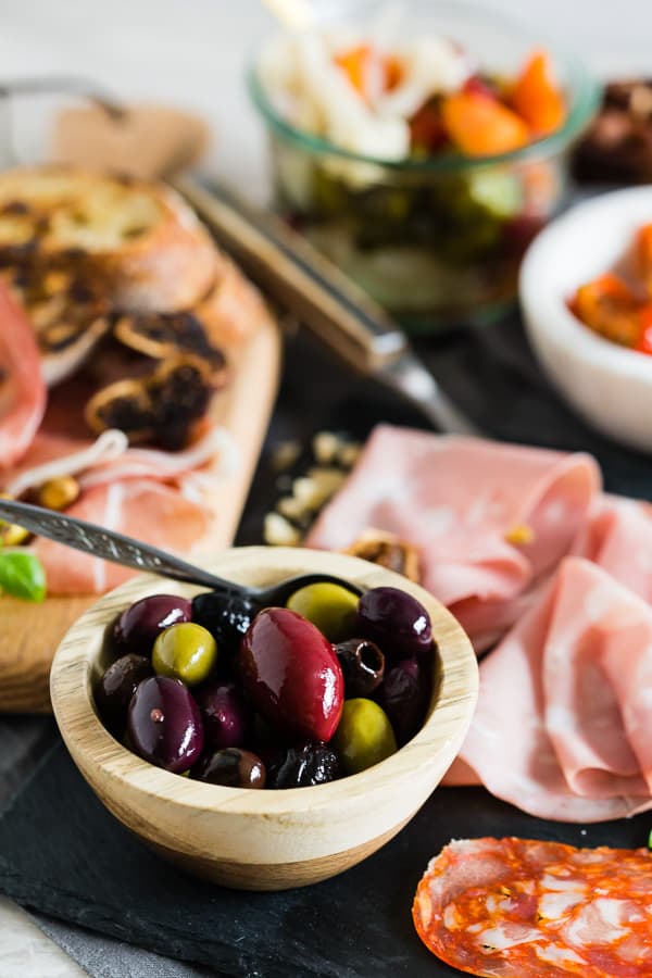 Bowl of olives with cured meats on a charcuterie board.