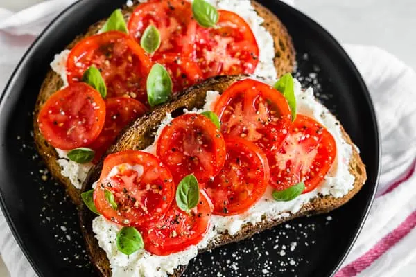 tomato ricotta toast served on a plate with fresh basil, salt, and pepper.
