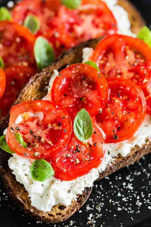 tomato ricotta toast on a plate sprinkled with kosher salt and black pepper. 