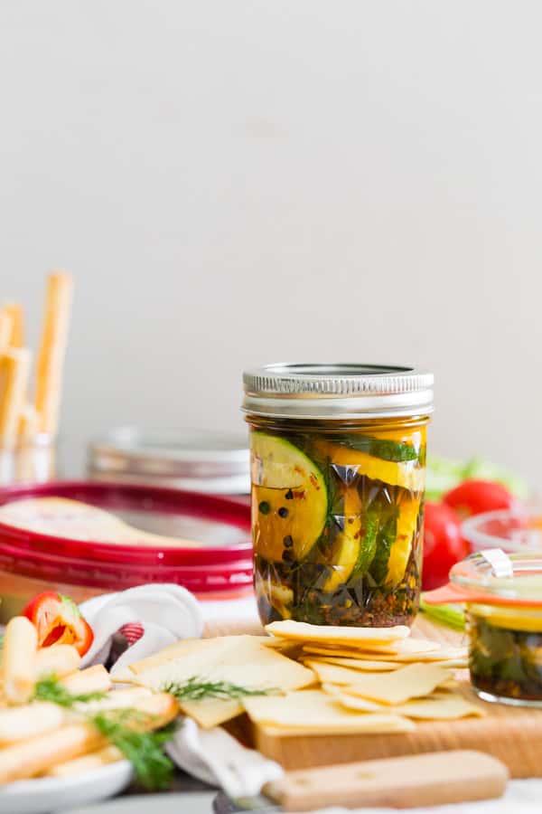 sweet and spicy zucchini pickles in a jar sitting on a hummus snack board
