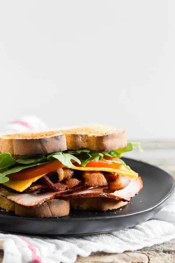 Close-up of sandwich with turkey, bacon, cheese, tomato and arugula.