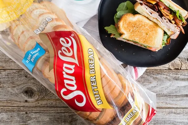 Loaf of Sara Lee bread next to a plate with a turkey BLT sandwich on it.
