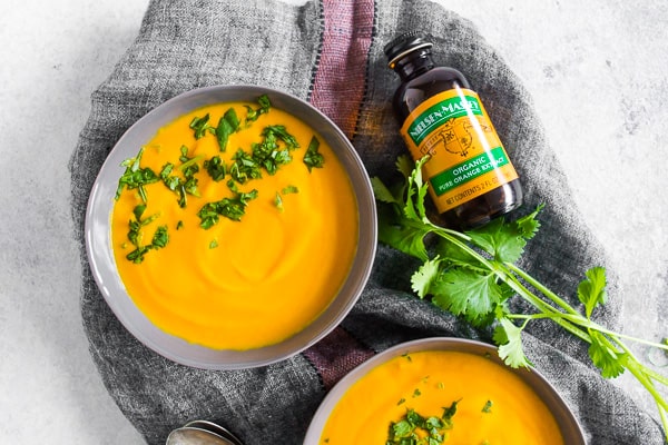Creamy Carrot Orange Soup in a bowl topped next to a bottle of orange extract. 