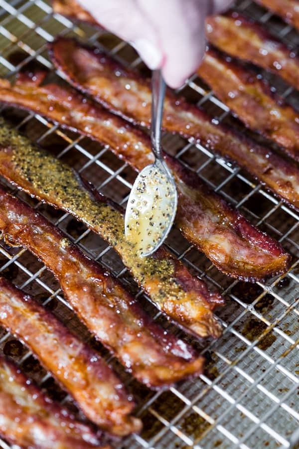 A spoon putting on pepper sauce to a cooked piece of bacon. 