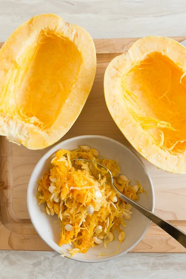 spaghetti squash cut in half on a cutting board with a bowl full of seeds