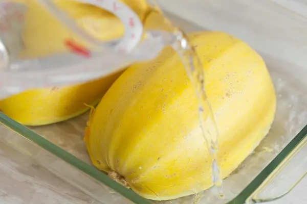 Spaghetti squash halves in a glass dish getting water poured in