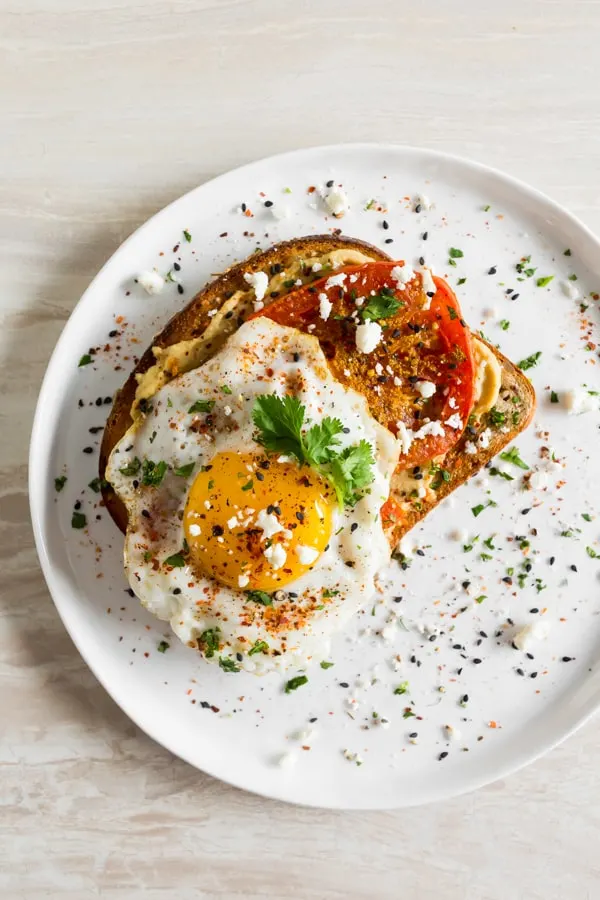 This shakshuka hummus toast is a healthy and flavorful way to start the day. Middle eastern spiced roasted tomatoes served on top of hummus toast with a runny egg, fresh herbs, and salty feta cheese.