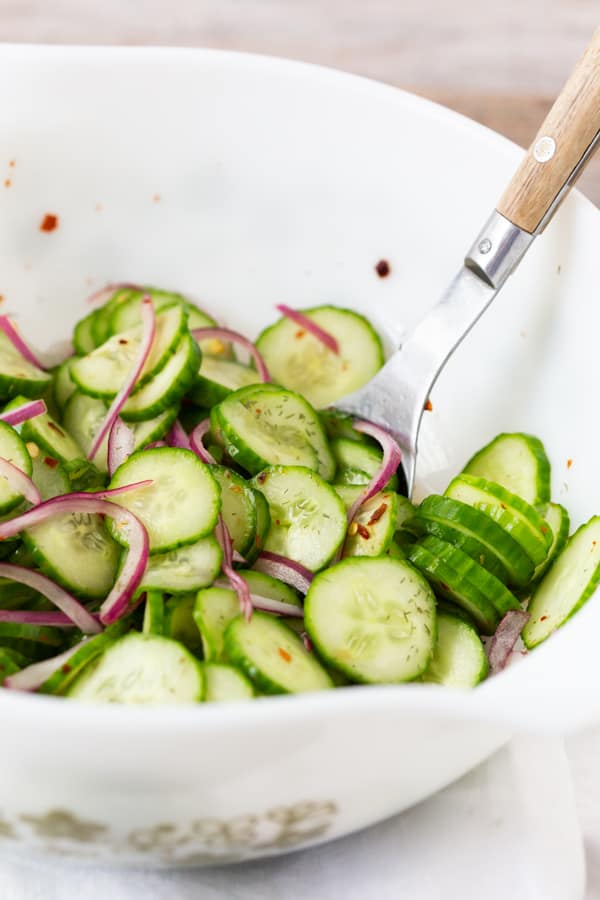 sliced cucumber salad with red onions in a white bowl