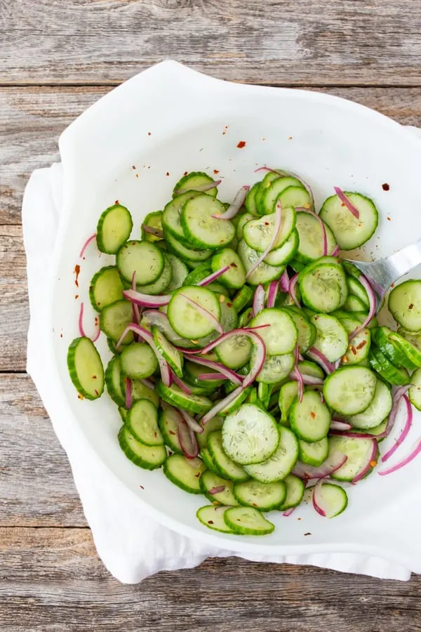 sliced cucumber salad with sliced red onion in a white bowl