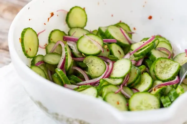 sliced cucumber salad in a white bowl with red onion