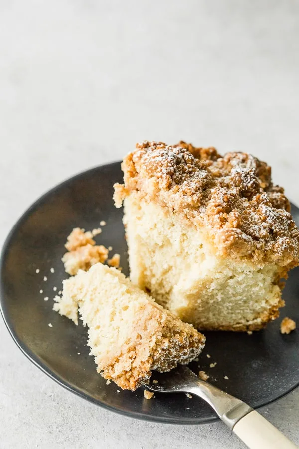 sourdough discard cinnamon crumb cake on a black pate with a bite sitting on a fork