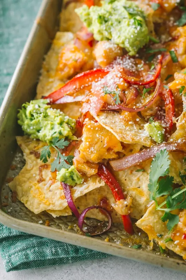 Sweet chili chicken nachos on a sheet pan topped with guacamole.