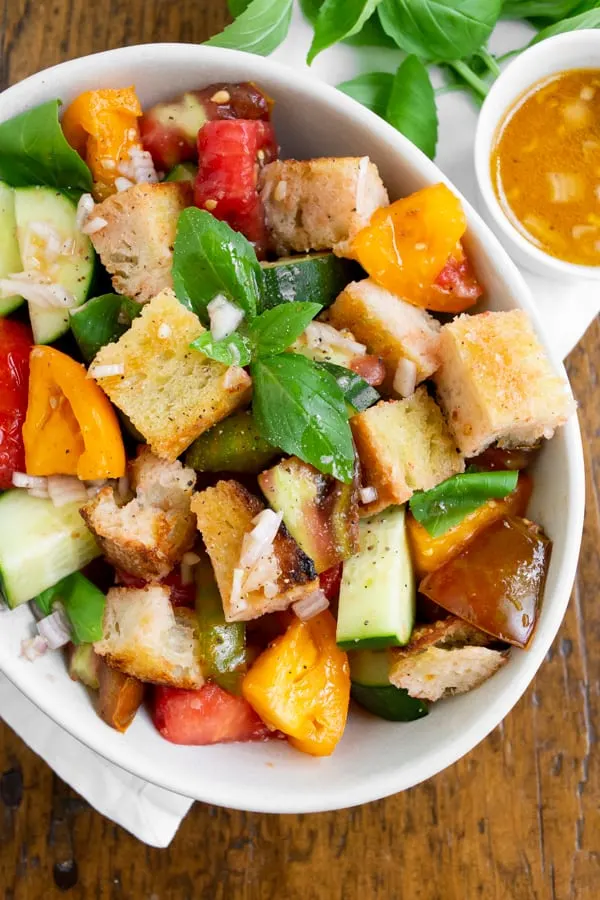 grilled sourdough panzanella salad in a white bowl with dressing on the side