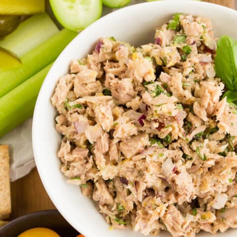 lemon herb tuna salad in a white bowl surrounded by cracker and vegetables