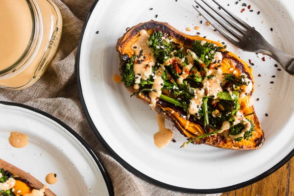 broccoli rabe and hummus stuffed sweet potatoes on a plate with extra dressing on the side
