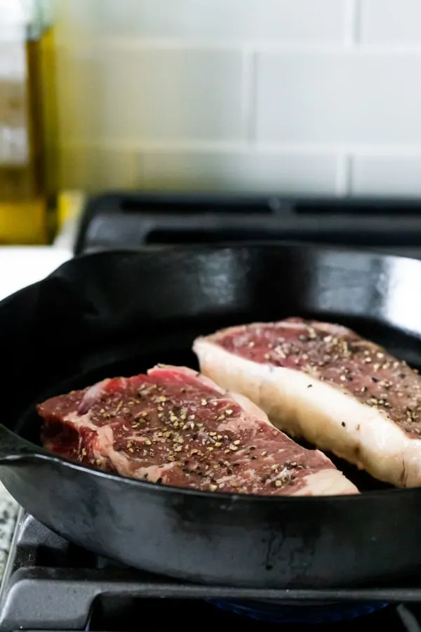 steaks cooking in a cast iron skillet on a stove